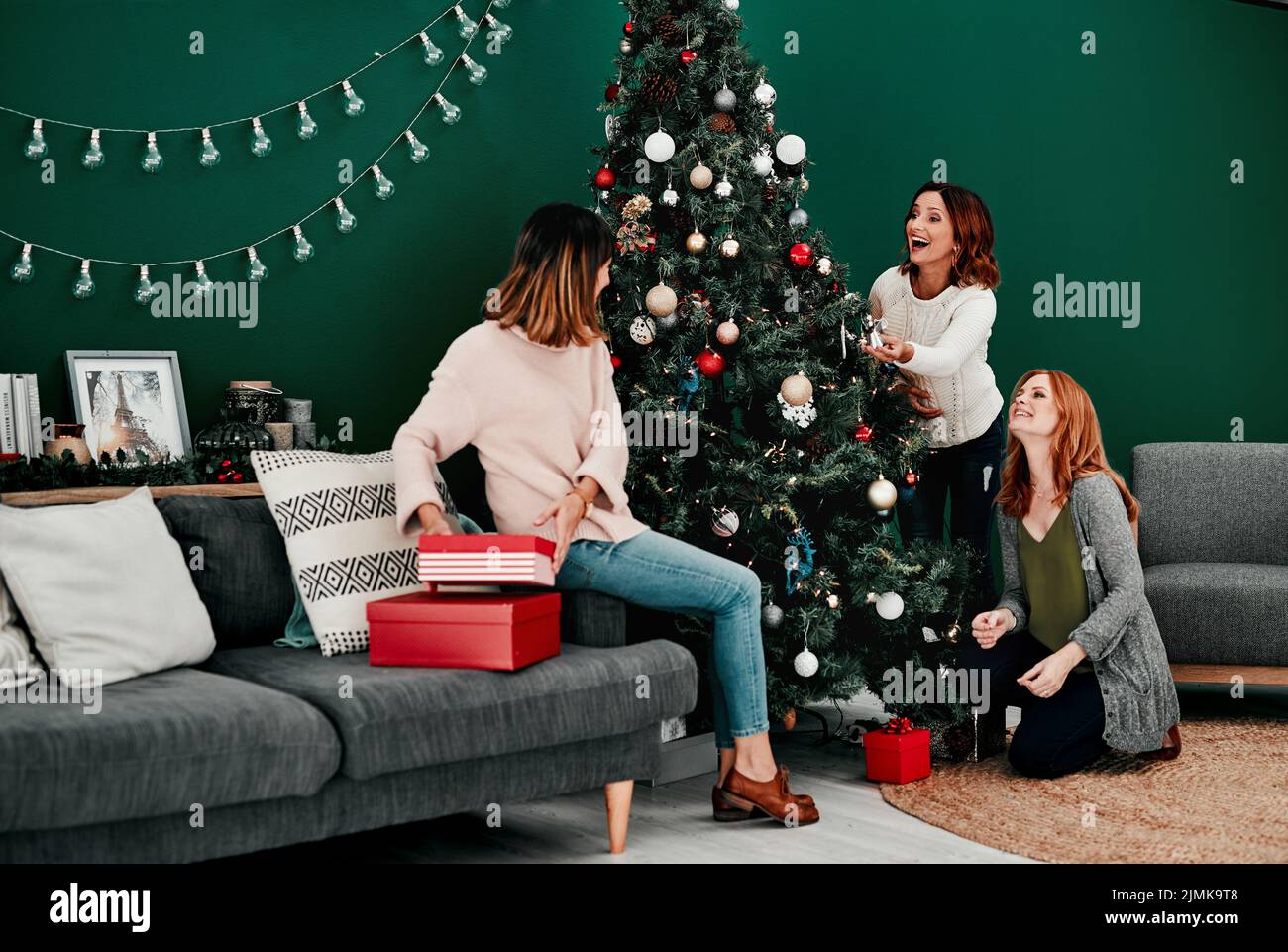 Der Baum sieht toll aus. Drei attraktive Frauen mittleren Alters schmücken einen Weihnachtsbaum zu Hause zusammen. Stockfoto
