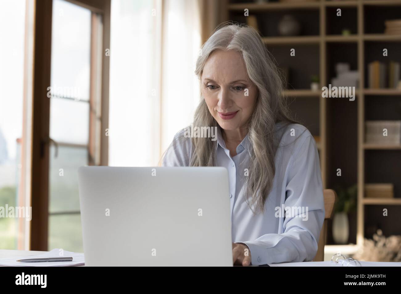 Nachdenkliche glückliche ältere ältere ältere Frau, die zu Hause einen Laptop verwendet Stockfoto