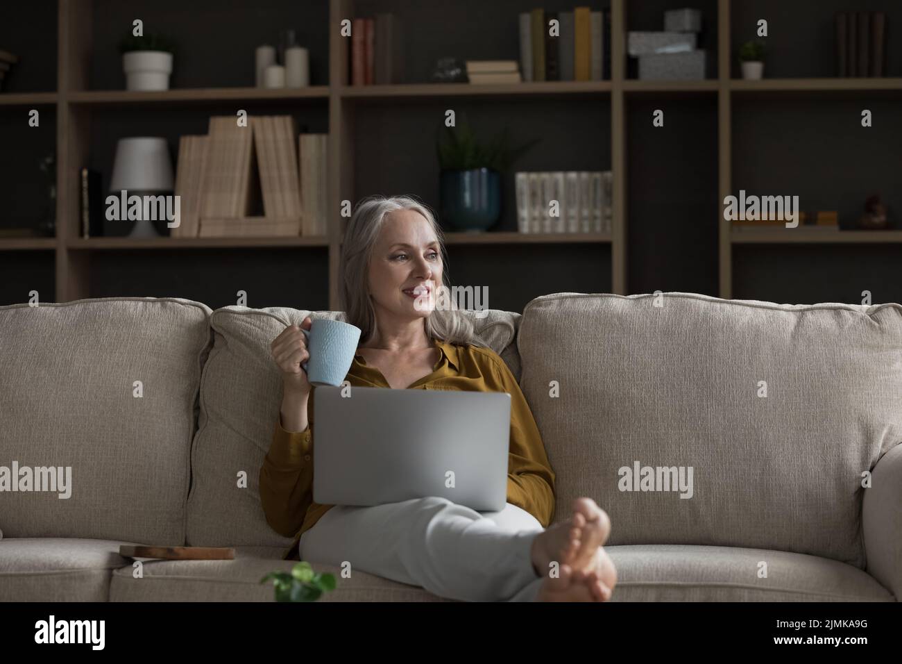 Glückliche verträumte nachdenkliche Rentnerin, die sich auf einem bequemen Sofa entspannt Stockfoto