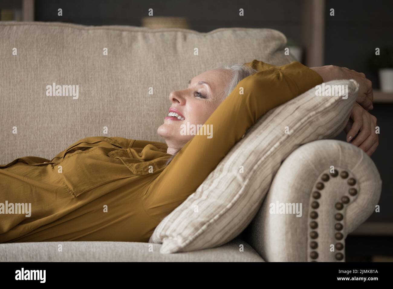 Fröhliche, fröhliche, reife Frau, die auf einer bequemen Couch liegt Stockfoto