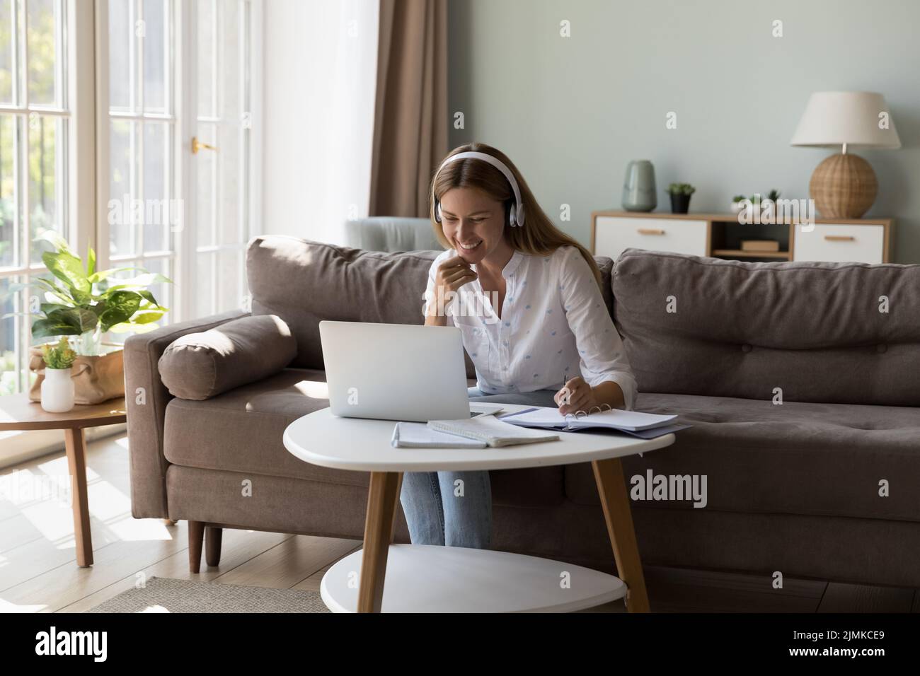 Frau mit Kopfhörern, die zu Hause bei einer Online-Lehrerin studiert Stockfoto