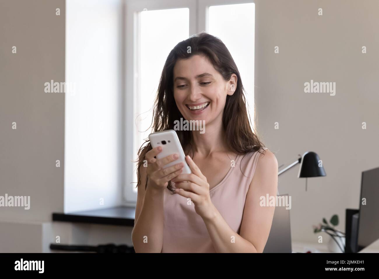 Büroangestellte, die mit dem Smartphone am Arbeitsplatz steht Stockfoto