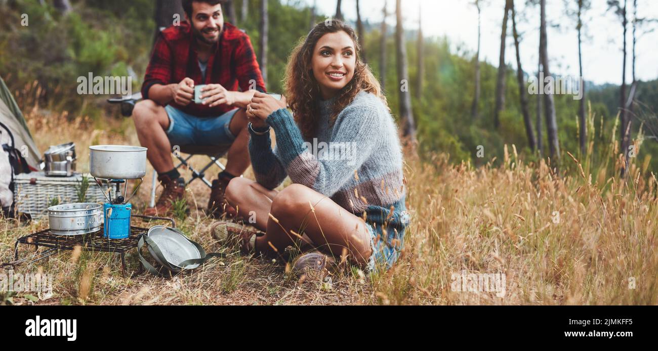 Fröhliches junges Paar, das während des Campens in der Natur Kaffee trinken kann. Glückliches junges Paar, das sich auf einem Campingurlaub gut Vergnügen kann. Stockfoto