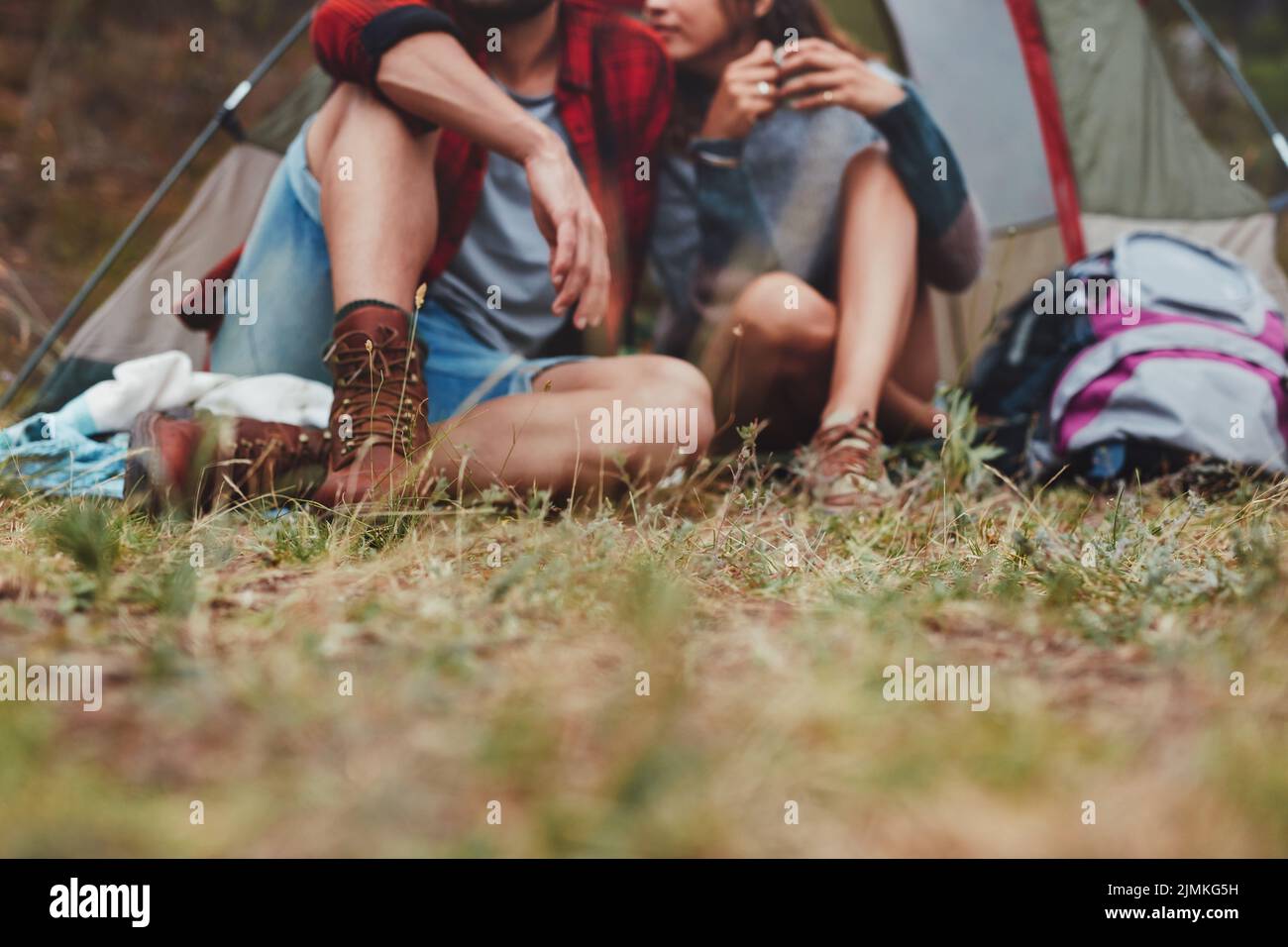 Romantisches junges Paar, das vor einem Campingzelt sitzt. Abenteuerliches junges Paar, das gemeinsam ihren Campingurlaub genießt. Stockfoto