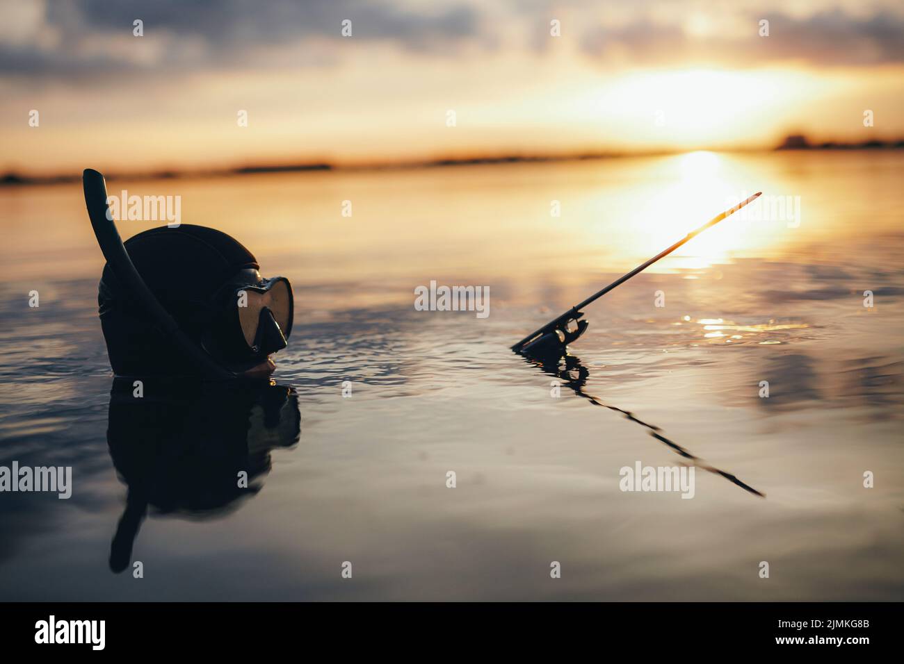 Speerfischertaucher mit einer Speergun, während er bei Sonnenuntergang in Meerwasser getaucht ist. Abenteuerlicher Taucher, der mitten im Meer nach Fischen jagt. Stockfoto