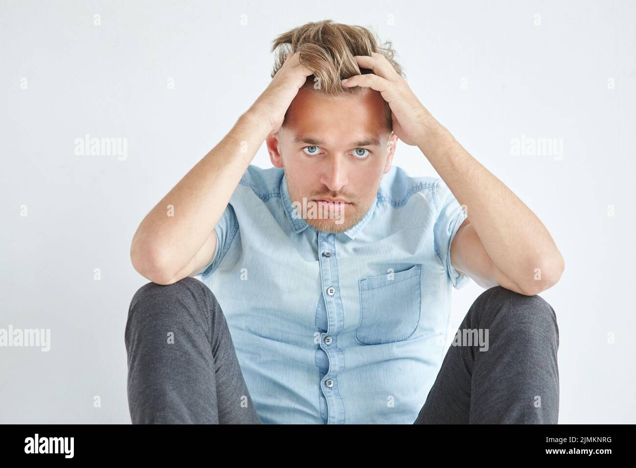 Brutaler Mann in einem Hemd mit kurzen Ärmeln sitzen auf dem Boden, unter dem Blick der Stirn, hielt seinen Kopf Stockfoto