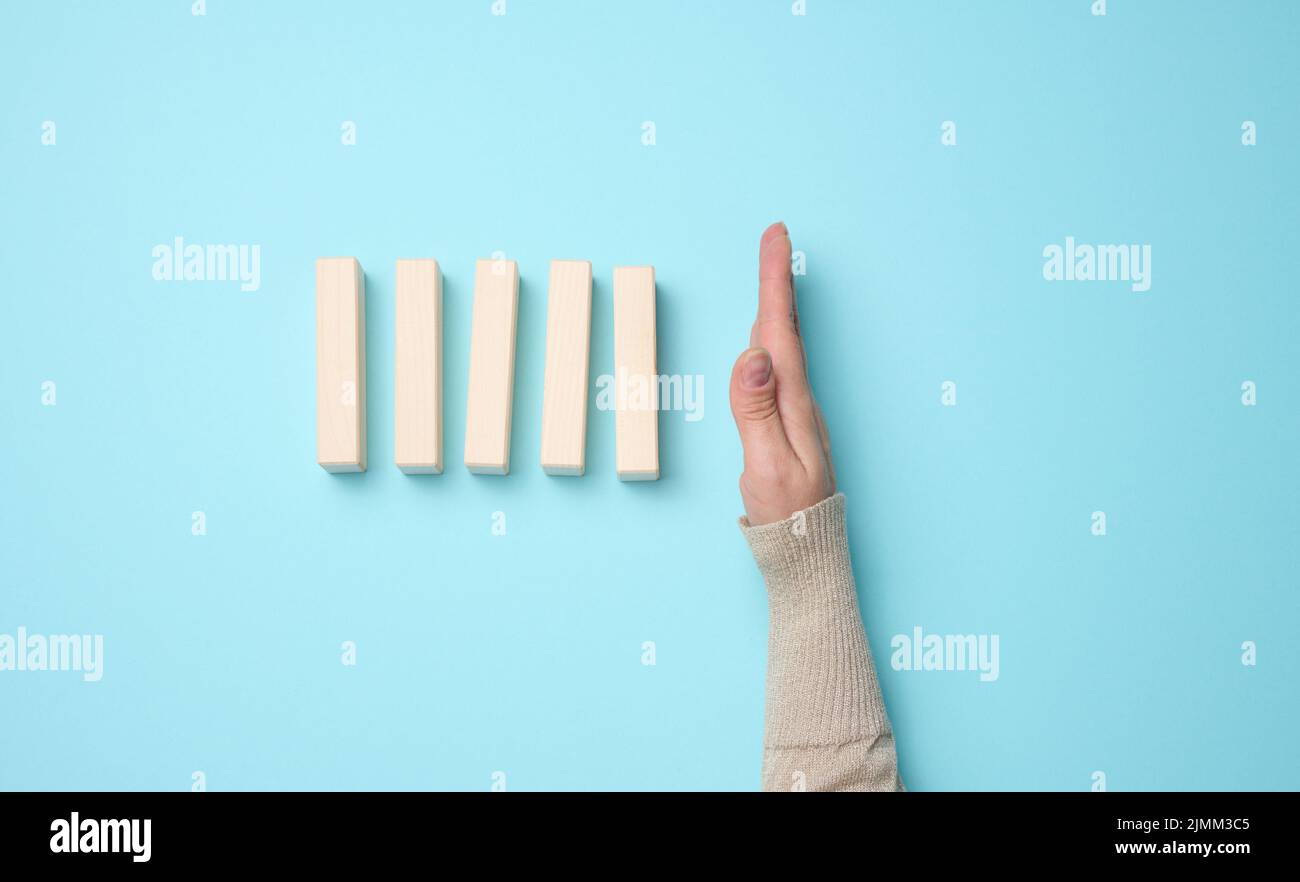 Hand stoppt den Fall von Holzblöcken auf einem blauen Hintergrund. Konzept einer starken und mutigen Persönlichkeit, die standin der Lage ist Stockfoto