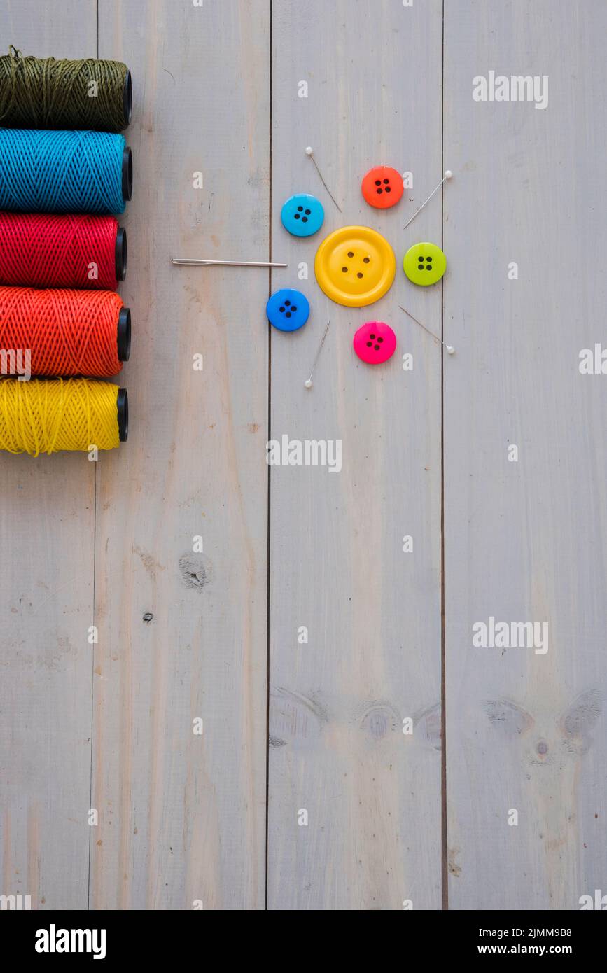 Bunte Garnspulen mit dekorativen Nadeln Stecknadeln bunte Knöpfe Holzschreibtisch Stockfoto