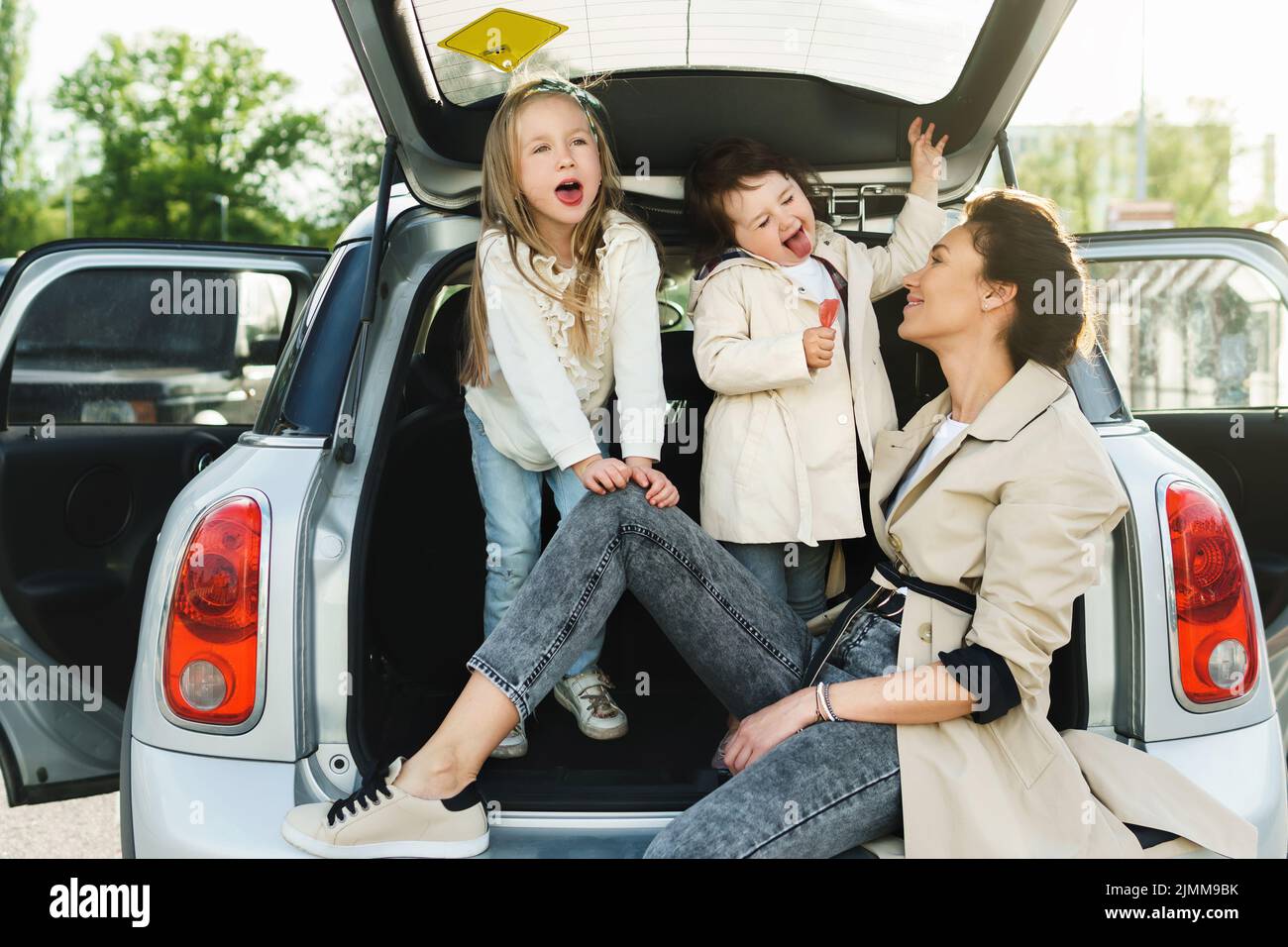 Die junge Mutter und ihre liebenswerten Dauthers sitzen in einem Kofferraum. Stockfoto
