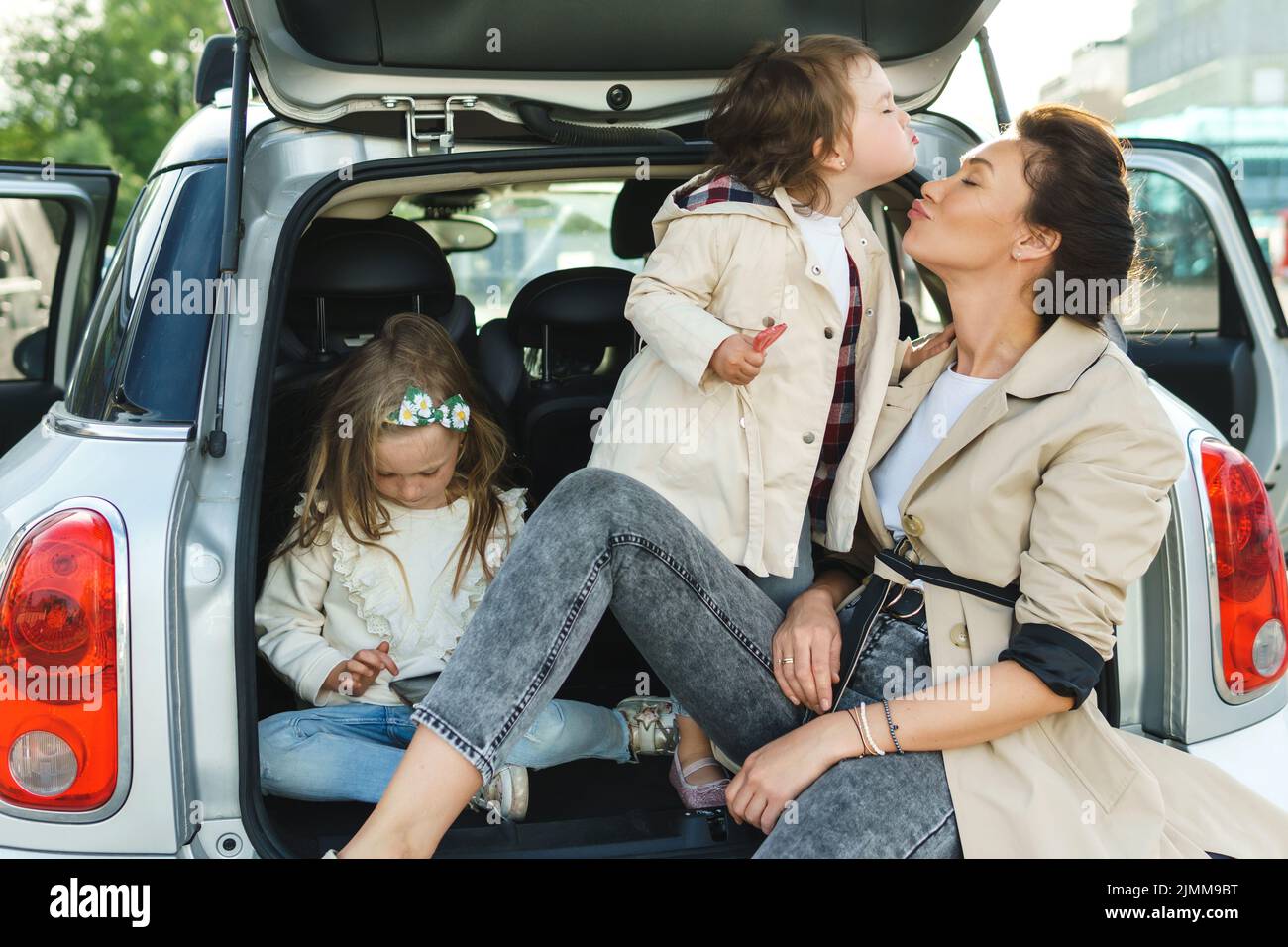 Die junge Mutter und ihre liebenswerten Dauthers sitzen in einem Kofferraum. Stockfoto