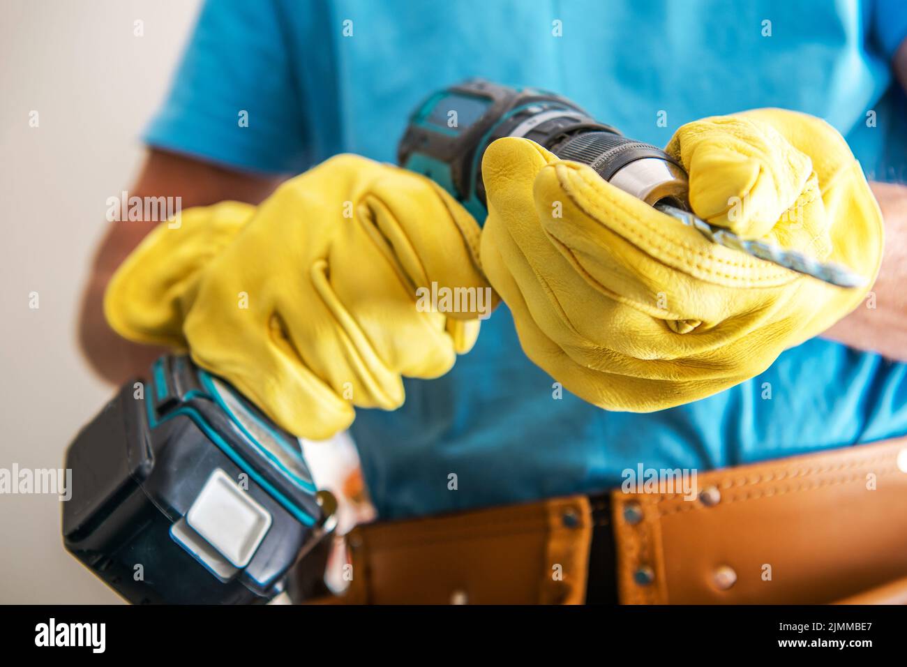 Nahaufnahme der elektrischen Bohrmaschine in den Händen eines professionellen Bauarbeiters mit gelben Schutzhandschuhen. Thema „Professionelle Elektrowerkzeuge“. Stockfoto