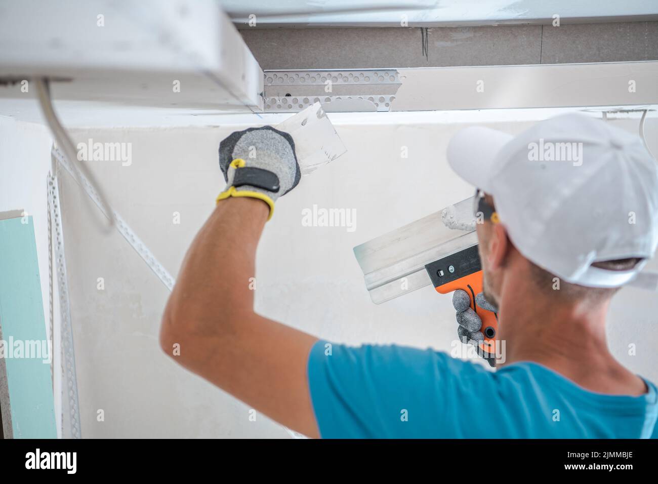 Rückansicht des kaukasischen Arbeiters, der die Wand während der Renovierungsarbeiten in der neu erbauten Wohnung mit Gipsputzen füllte. Industriedesign. Stockfoto