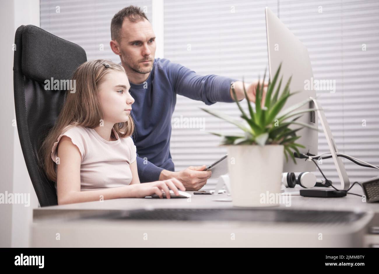 Kaukasische Familie von Vater und Tochter, die vor dem Computer sitzen und den Monitor betrachten. Stolzer Vater unterweist seine junge Tochter im uns Stockfoto