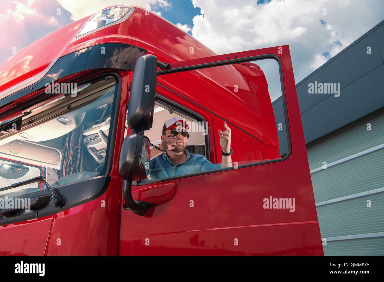 Kaukasischer Trucker in seinem 30s sitzenden in der roten Kabine seiner Semi-Truck-Gestik, während er ein hartes Gespräch über ein Citizens Band Radio geführt hat. Stockfoto
