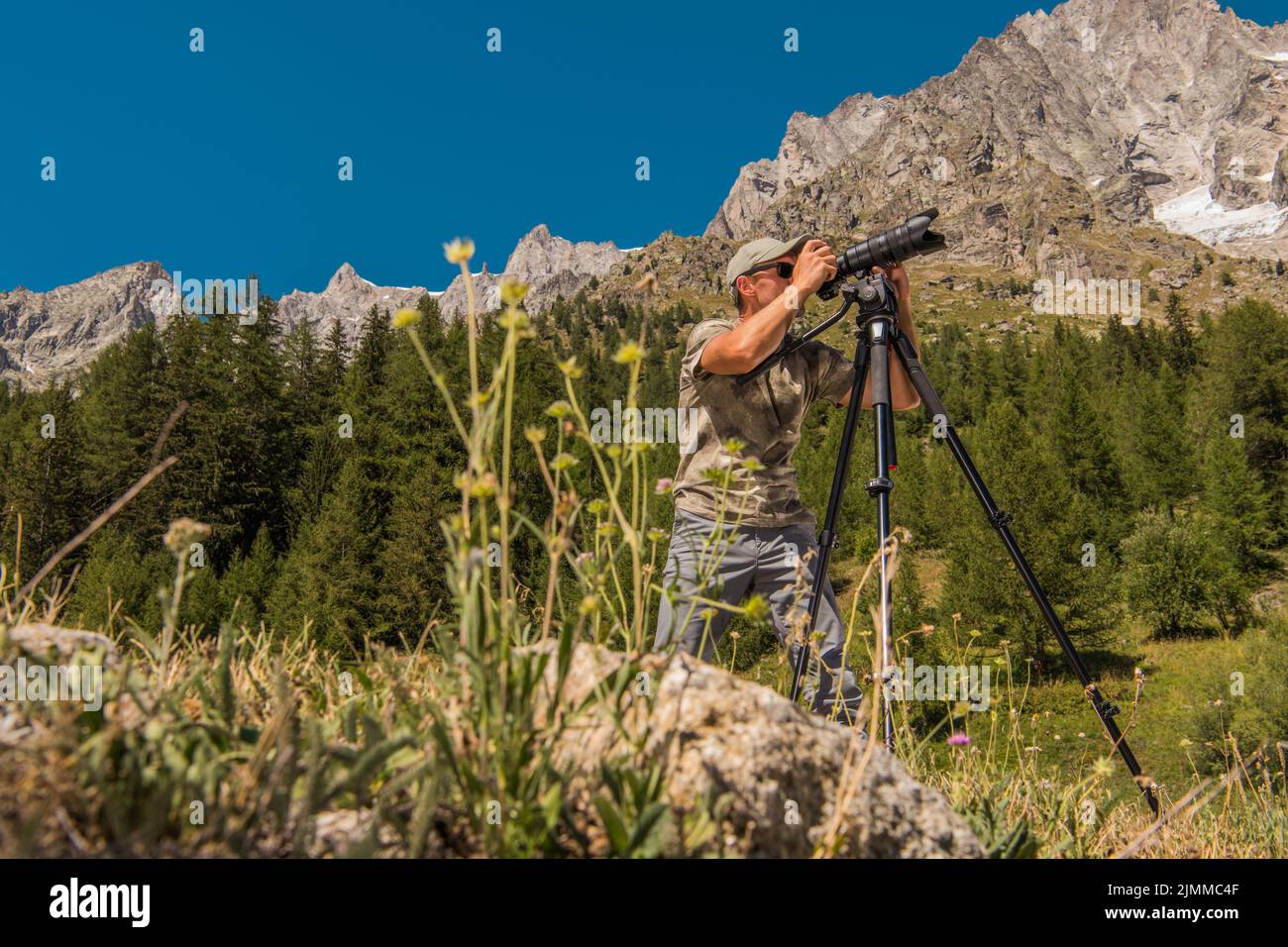Wanderfotograf aus der Natur, der mitten in der malerischen Landschaft steht und mit seiner Kamera auf einem Stativ ein Foto der Alpen fotografiert. Stockfoto