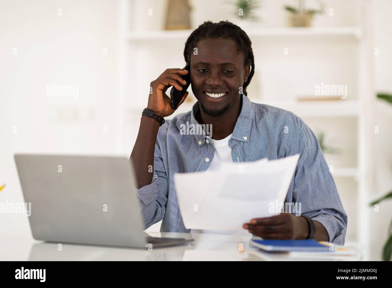 Afroamerikanischer Mann, Der Am Mobiltelefon Spricht Und Mit Papieren Im Büro Arbeitet Stockfoto