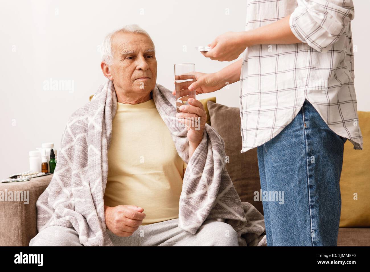 Die Frau gibt ihrem kranken älteren Großvater Medikamente Stockfoto