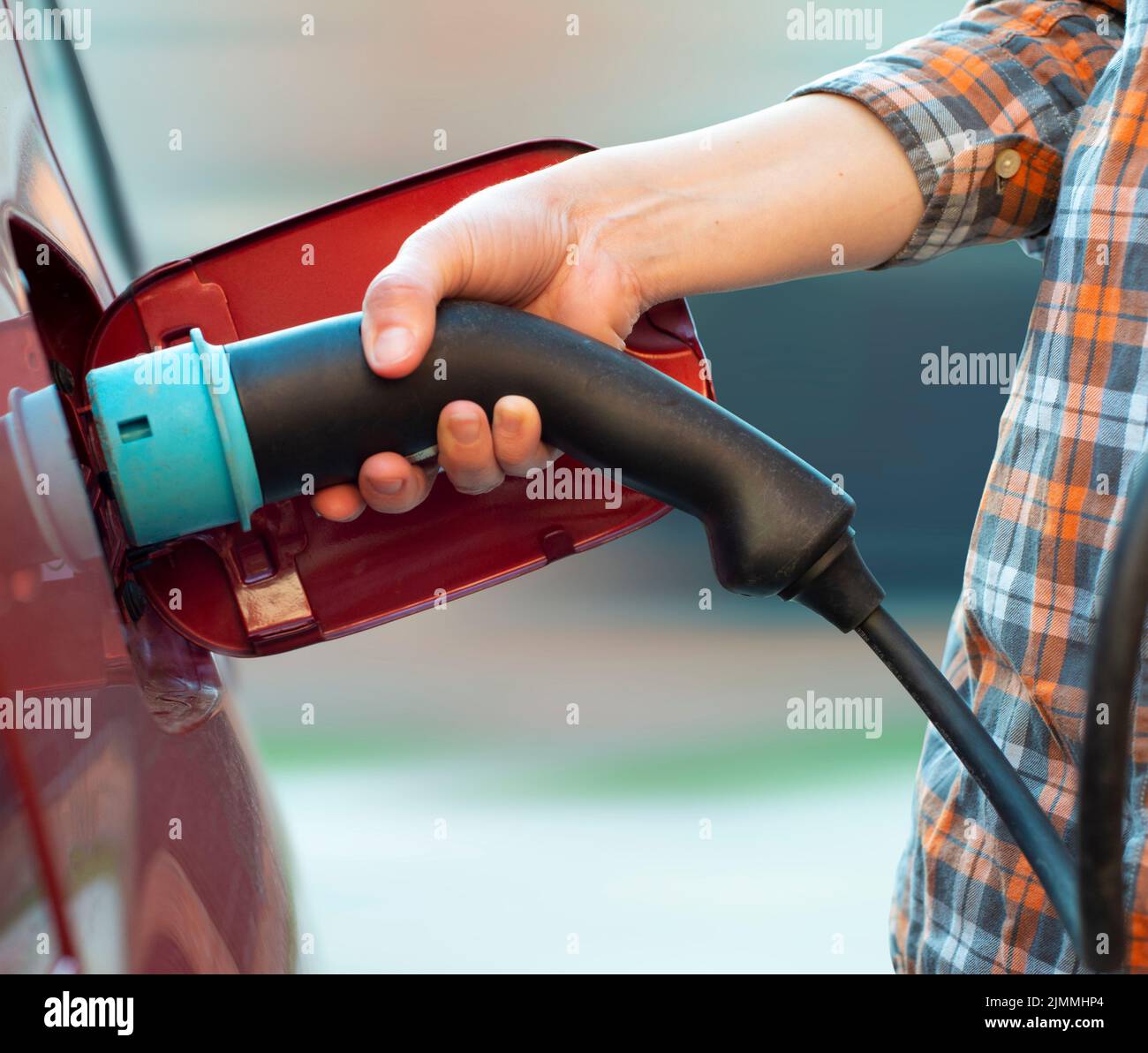 Das weibliche Modell steht neben einem Elektroauto und hält einen Ladestecker Stockfoto