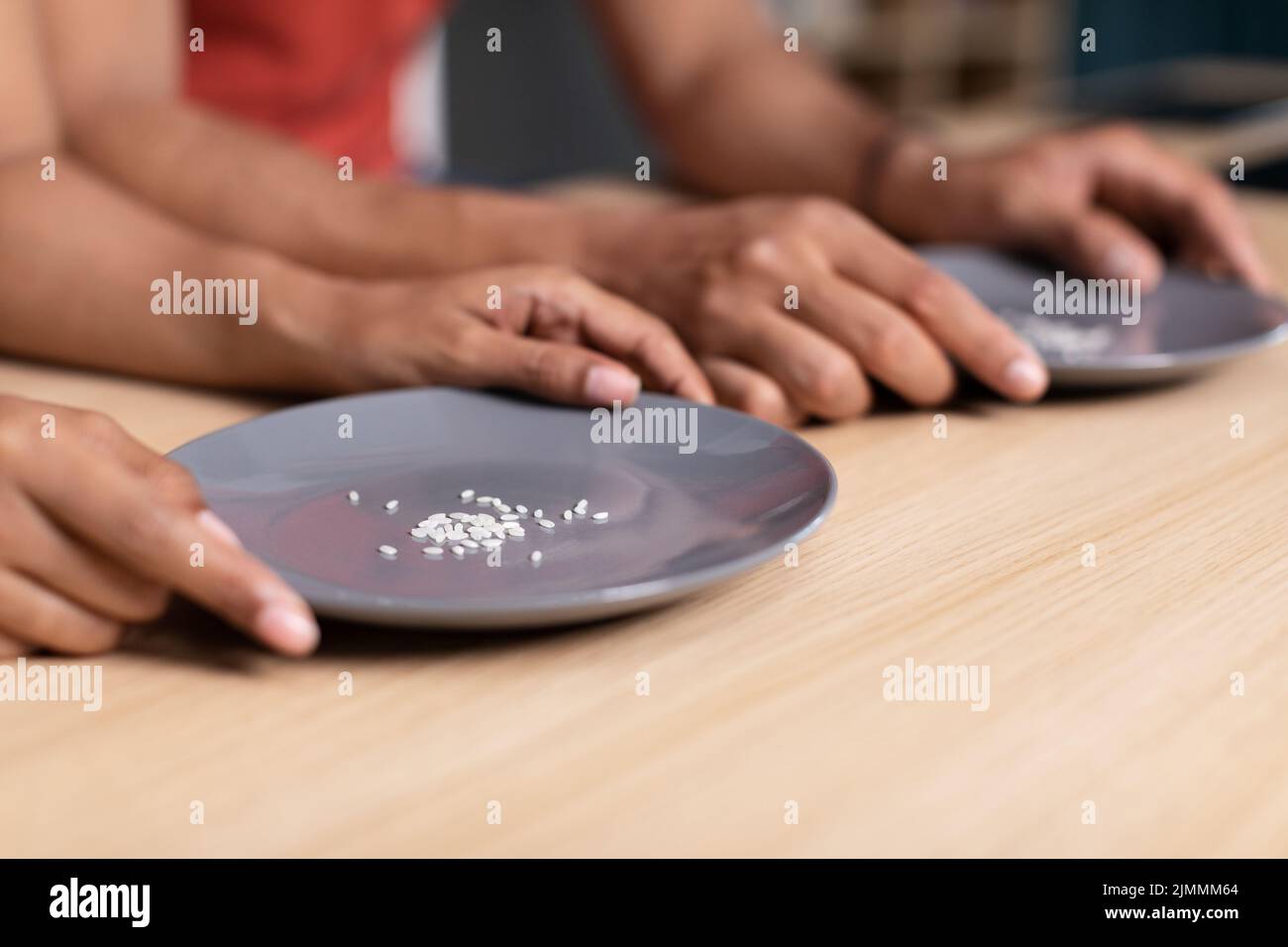 Hände junger schwarzer Familie halten Teller mit einigen Körnern Reis am Tisch in der Küche, abgeschnitten Stockfoto