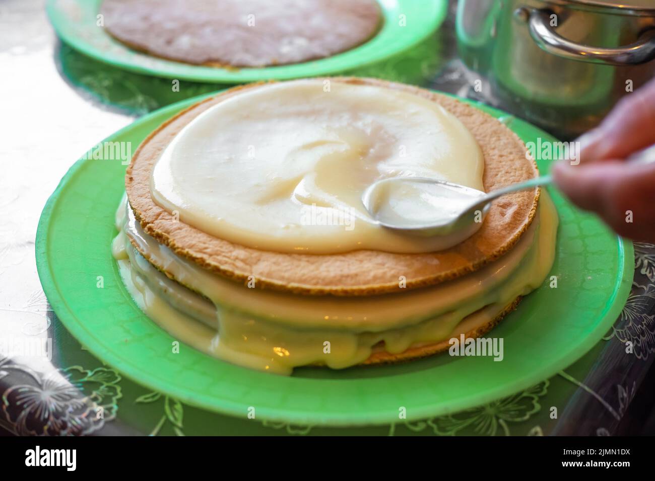 Kochen hausgemachten Kuchen. Eine Frau bedeckt Backkuchenschichten mit Pudding. Stockfoto