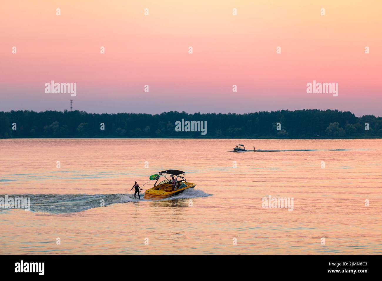 Ein Boot zieht eine Person auf einem Wakeboard über die Wellen. Wakeboarding bei Sonnenuntergang. Stockfoto