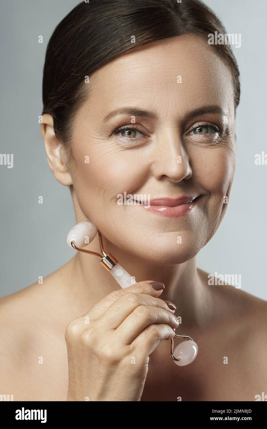 Schöne Frau mittleren Alters mit Rosenquarz Derma Roller Stockfoto