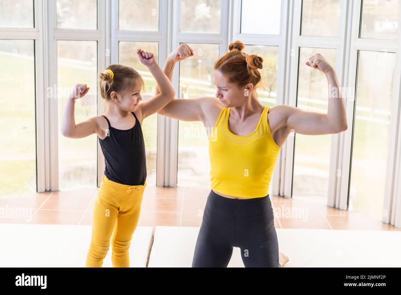 Junge fit Mutter und ihre Tochter in passenden Kleidern, zeigen Muskeln. Fitness-Motivation Stockfoto