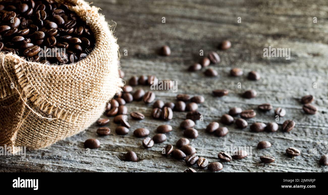 Kaffeebohnen auf einem rustikalen Tisch verteilt mit einem vollen Beutel auf der linken Seite. Stockfoto