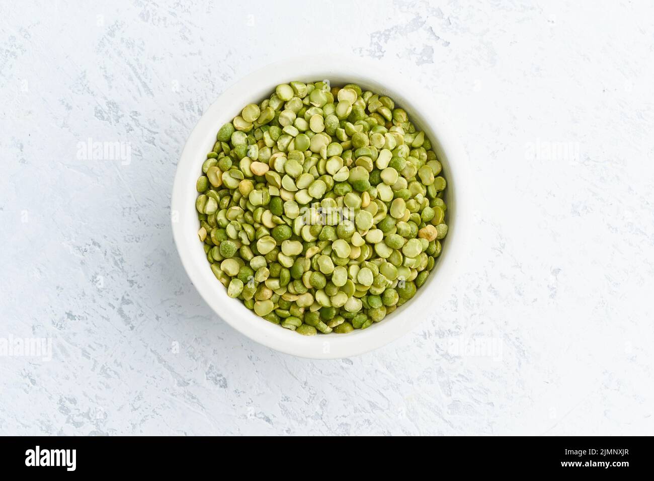 Grüne Erbsen in weißer Schüssel auf weißem Hintergrund. Getrocknetes Getreide in Tasse, veganes Essen. Draufsicht, Nahaufnahme. Stockfoto