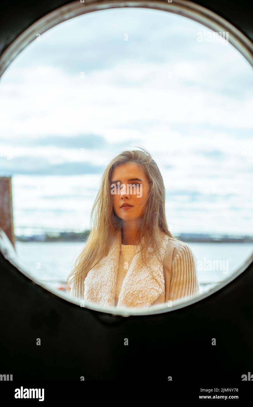 Das Gesicht des jungen Mädchens in runden Rahmen Fenster auf dem Hintergrund des Meeres, Ozean, am Wasser. Porträt im Kreis, hinterleuchtet, vertikal Stockfoto