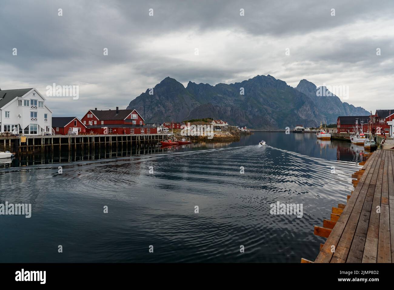 Norwegische Seestücke, Stadtbild der Stadt Henningsvaer, ein kleines Boot bewegt sich zwischen Halbinseln, Segelboot, felsige Küste mit Drama Stockfoto