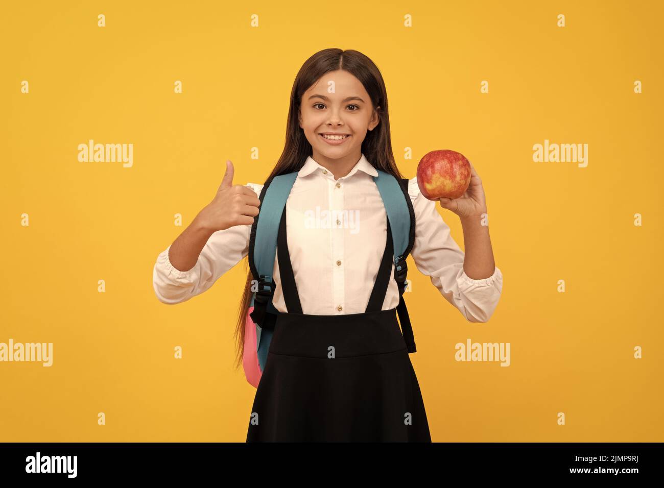 Glückliches Mädchen Kind geben Daumen nach oben halten Apfel und Schultasche gelben Hintergrund, Bildung Stockfoto