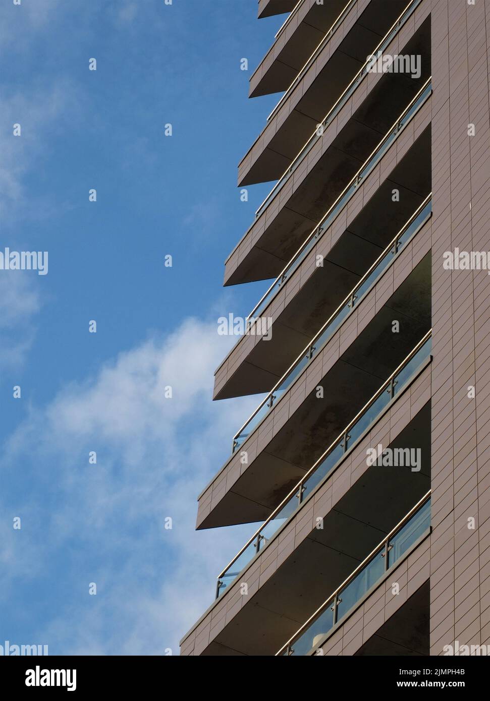 Die angewinkelten Balkone mit Glasgeländern befinden sich in einem modernen Apartmentgebäude, das von einem blau bewölkten Himmel umgeben ist Stockfoto