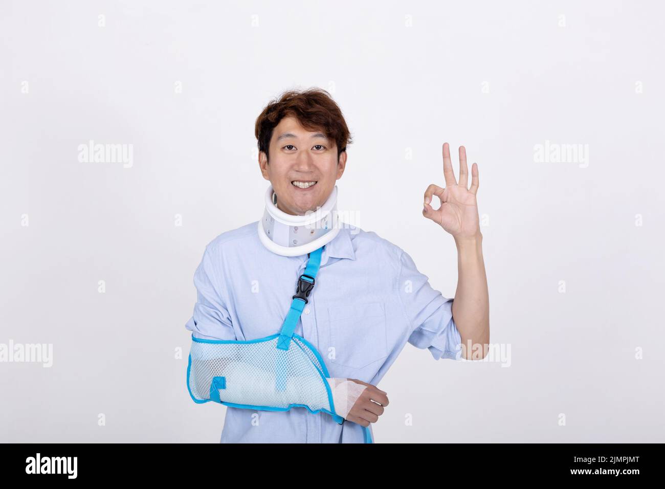 Porträt eines lächelnden asiatischen Mannes mit gebrochenem Arm und Hals Gefühl zeigt okay Zeichen Geste isoliert auf weißem Hintergrund Kopie Raum Stockfoto