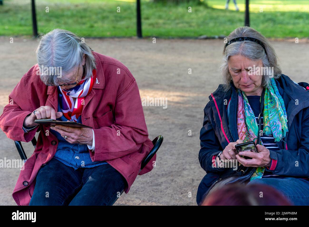 Zwei ältere Frauen, die Mobiltelefone/Smartphones nutzen, warten auf den Beginn der Queen's Birthday Parade, Platinum Jubilee Celebrations, The Mall, London, Großbritannien. Stockfoto