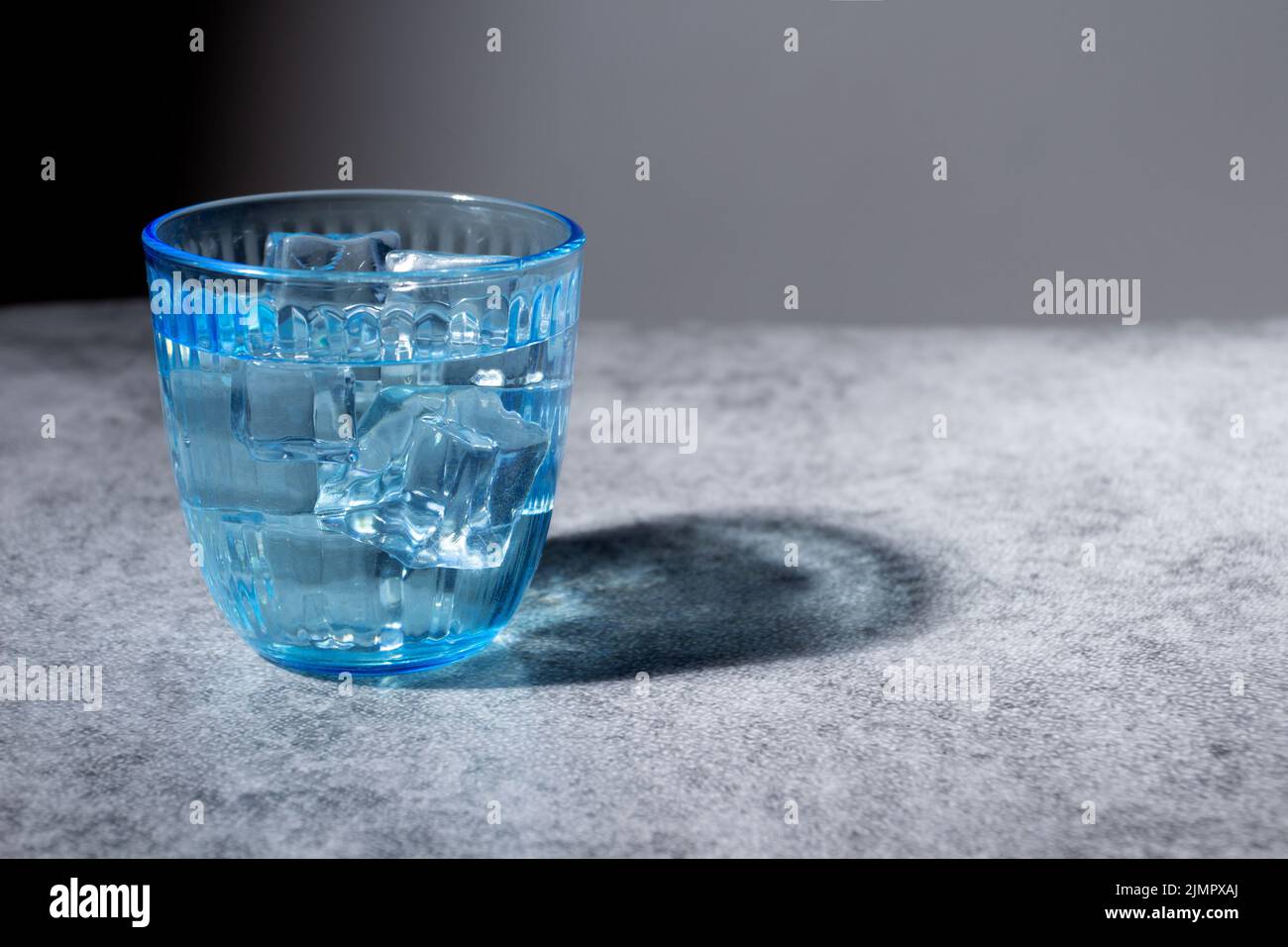 Dekoratives blaues Glas mit Wasser und Eis auf rustikaler Oberfläche Stockfoto