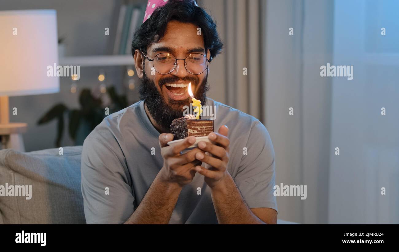 Portrait fröhlich fröhlich arabisch indisch bärtig Mann in Gläsern in festlicher Mütze zu Hause Abend feiert Jubiläum Spaß mit kleinen Kuchen halten Stockfoto