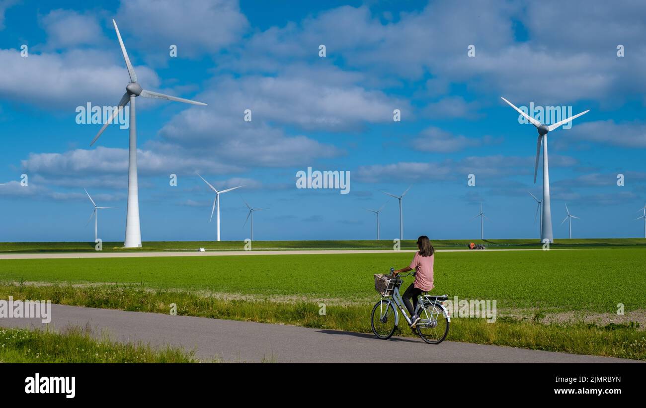 Junge Frau elektrische grüne Fahrrad von Windmühle Bauernhof , Windmühlen isoliert an einem schönen hellen Tag Niederlande Flevoland Nein Stockfoto