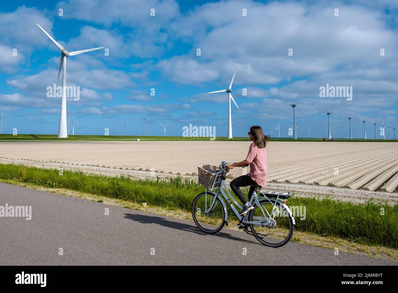 Junge Frau elektrische grüne Fahrrad von Windmühle Bauernhof , Windmühlen isoliert an einem schönen hellen Tag Niederlande Flevoland Nein Stockfoto