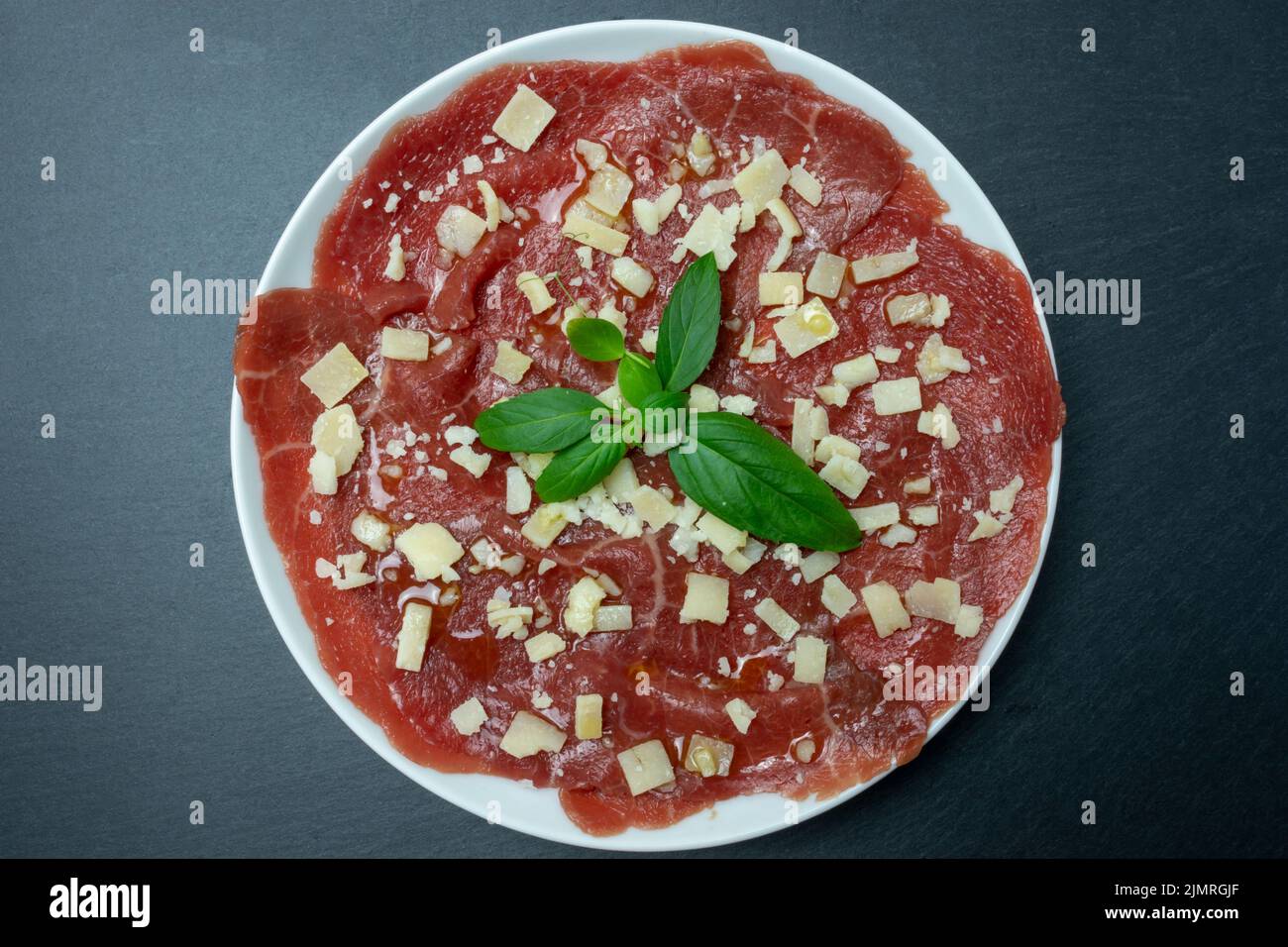 Marmorierte Rindercarpacio mit Basilikum und Parmesan. Schwarzer Hintergrund. Draufsicht. Stockfoto