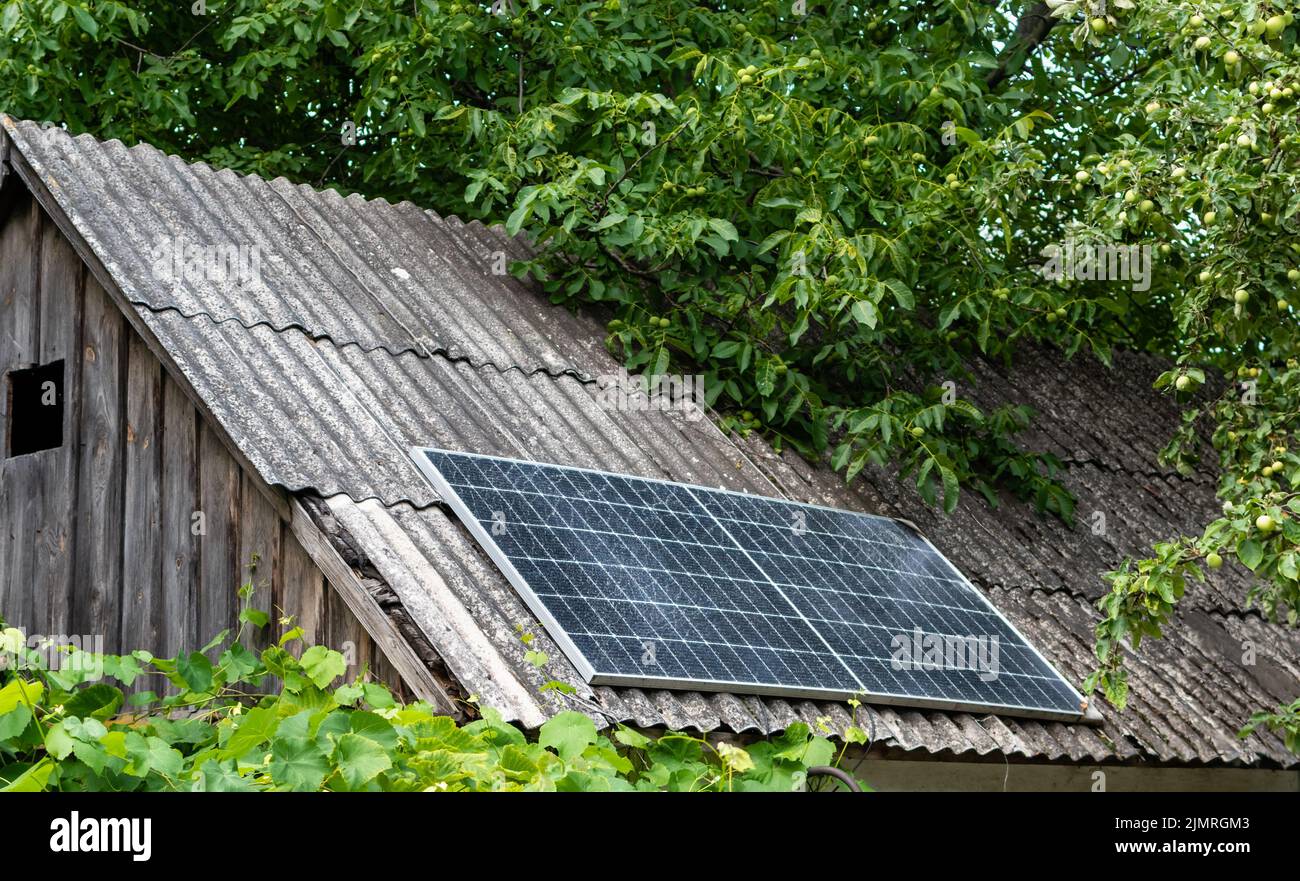 Solarpanel auf dem Dach der alten Scheune im Dorf in dichtem Grün der Blätter Stockfoto