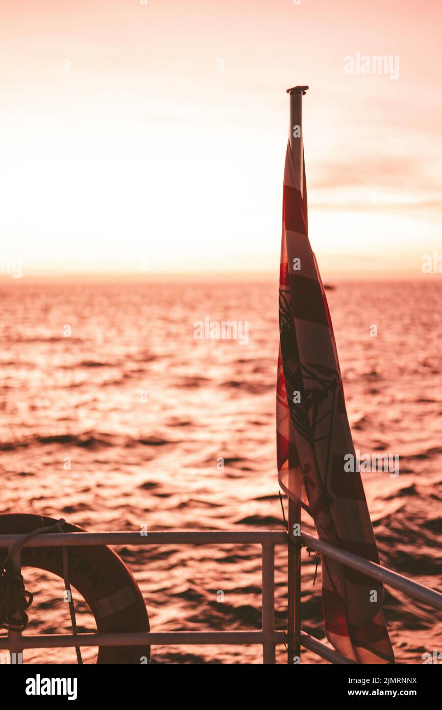 Flagge auf einer Bootstour bei Sonnenuntergang auf dem Meer Stockfoto