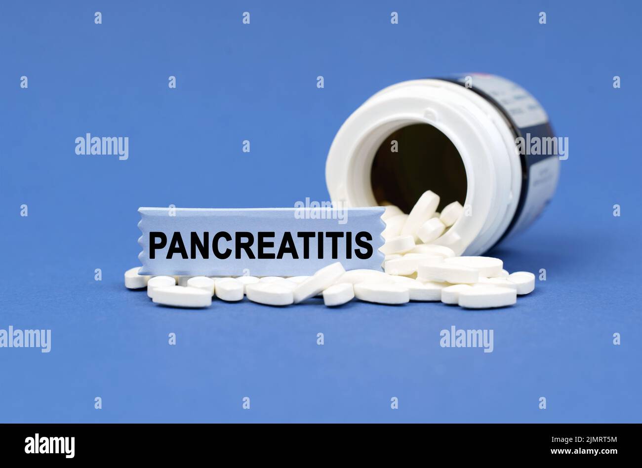 Medizinisches Konzept. Auf einer blauen Oberfläche liegt ein Glas Pillen und ein Schild mit der Aufschrift - PANKREATITIS Stockfoto