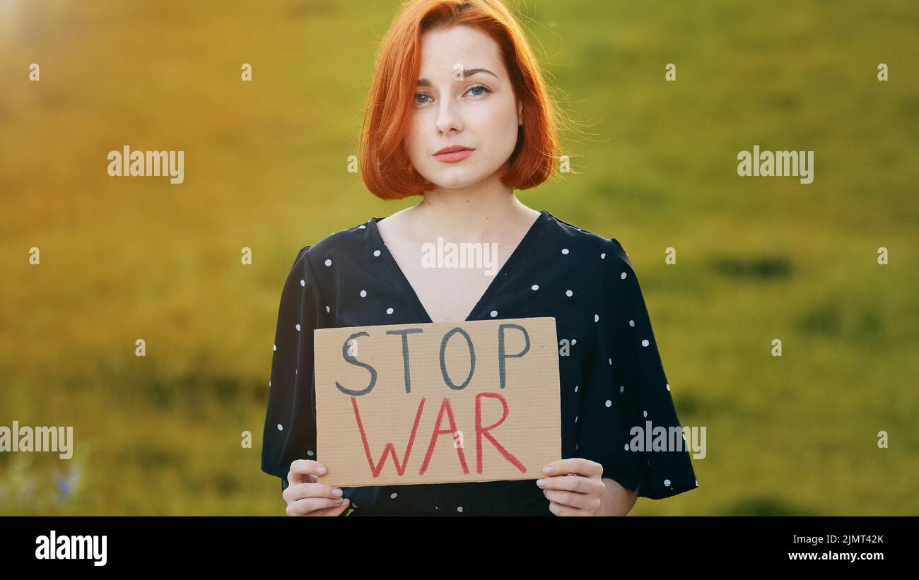 Unglückliche kaukasische junge Rotschopf-Aktivistin hält demonstrierende Banner mit Aufschrift STOP war traurig hübsches Mädchen steht im Freien in der Feldshow Stockfoto