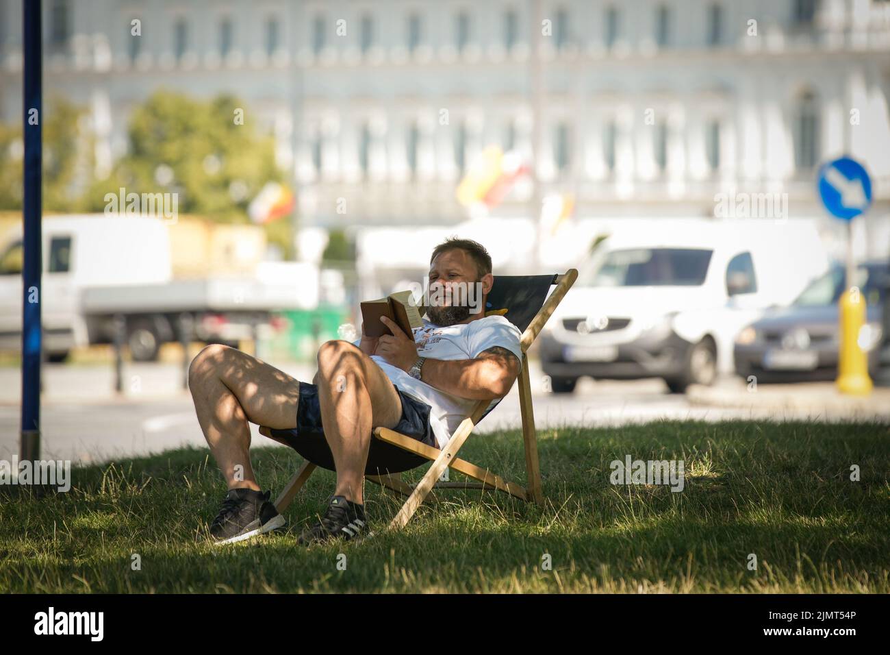 An einem heißen Tag in Warschau, Polen, am 7. August 2022, wird ein Mann gesehen, der auf einem Liegestuhl auf einem grasbewachsenen Fleck in der Nähe des geschäftigen Verkehrs ein Buch liest. Stockfoto