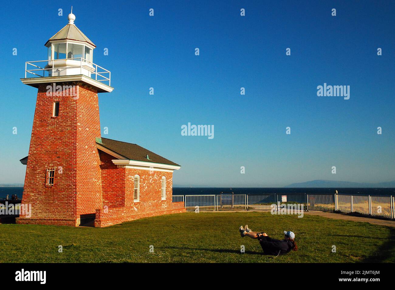 Eine junge Frau trainiert auf dem Rasen vor dem Abbott Memorial Lighthouse, bevor sie in der Nähe von Santa Cruz, Kalifornien, im Ozean surft Stockfoto