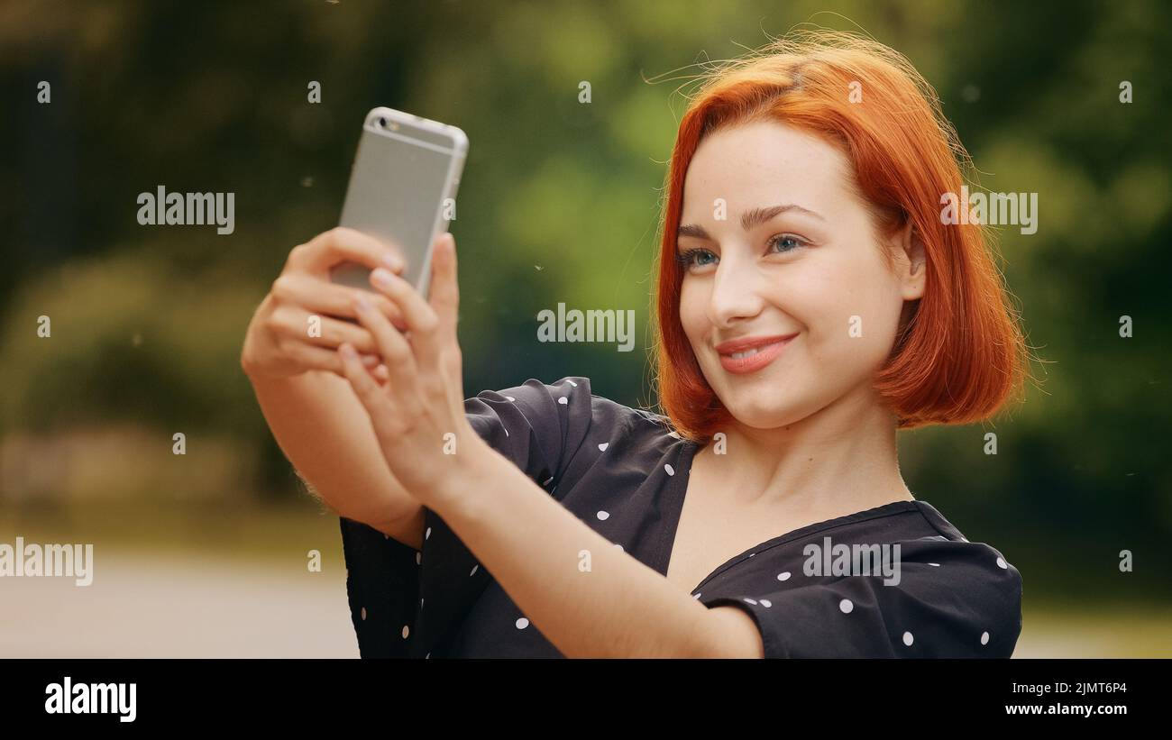 Portrait stilvolle schöne Mädchen kaukasisch attraktive rothaarige Frau blogger weibliches Modell steht draußen im Park hält Smartphone nimmt Selfie Foto auf Stockfoto