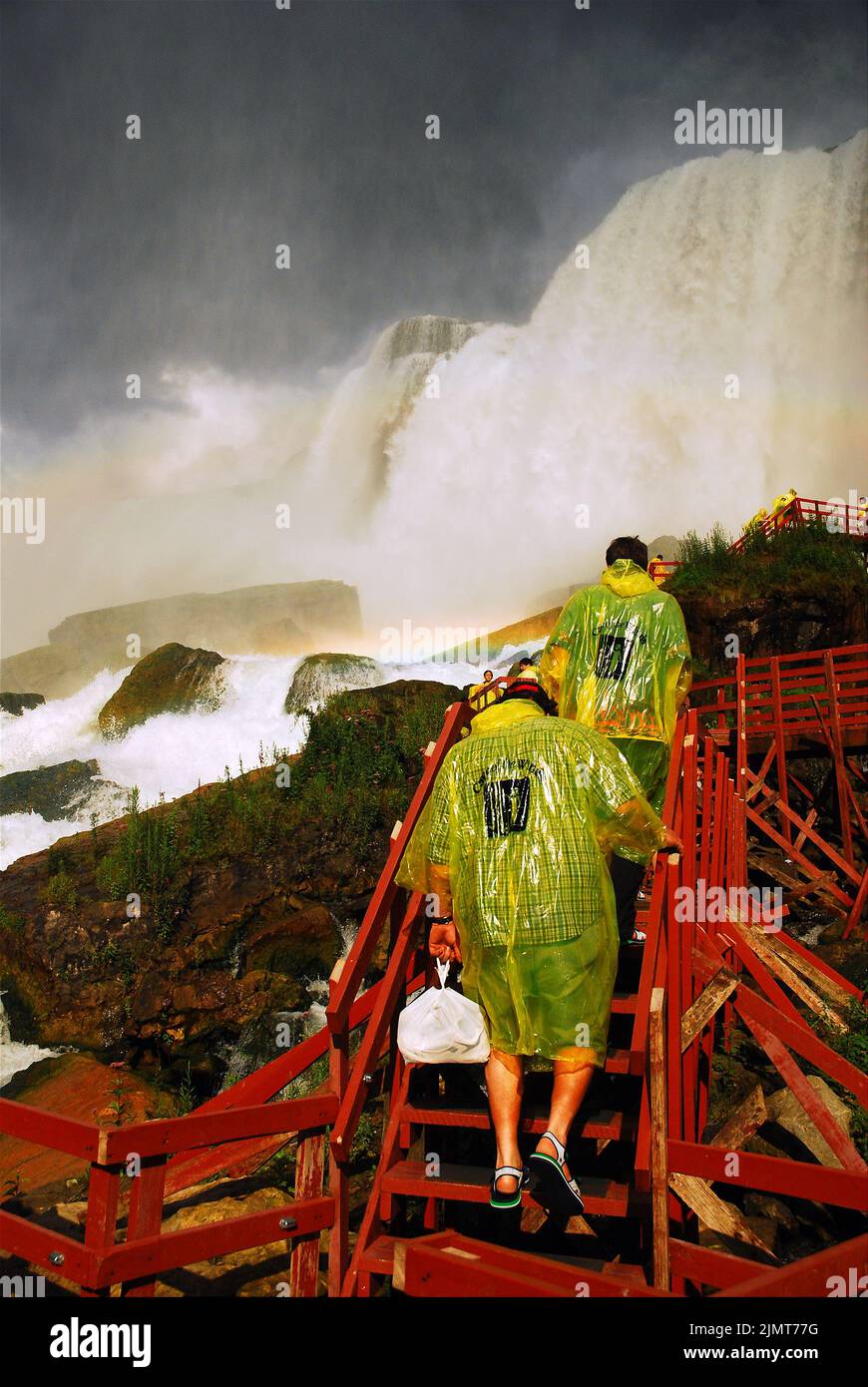 Zwei Personen, die gelbe Regenmantel-Slips tragen, steigen die Holztreppen und Decks hinauf, um die Bridal Veil Falls in Niagara Falls, New York, aus nächster Nähe zu sehen Stockfoto
