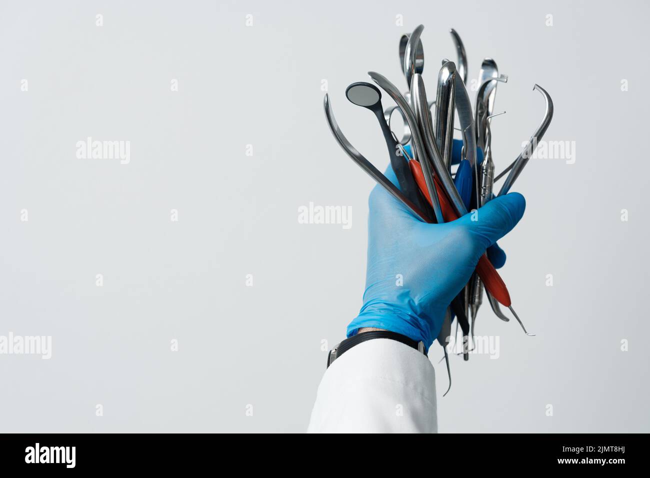 Die Hand des Zahnarztes in einem blauen Handschuh hält eine Reihe von zahnärztlichen Instrumenten, Zahnspiegel, Pinzette, Sondenhaken. Werbung für Zahnmedizin und zahnärztliche Dienstleistungen Stockfoto