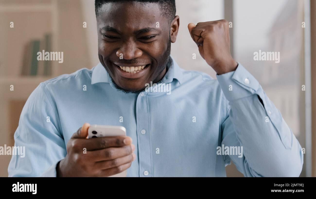 Afrikanischer junger Mann überrascht erhalten gute Nachricht auf Handy gewinnen Online-Wette freuen Weitergabe mobile Spiel Ebene männlich amerikanischen Kerl Geschäftsmann fühlen Stockfoto